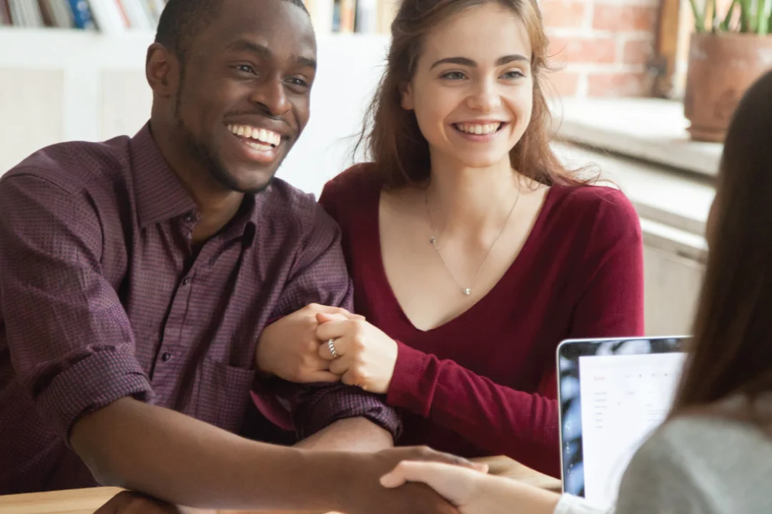 young couple smiling and shaking hands with female loan provider