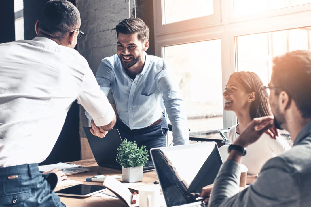 team of coworkers standing up to shake hands while other team members look and smile