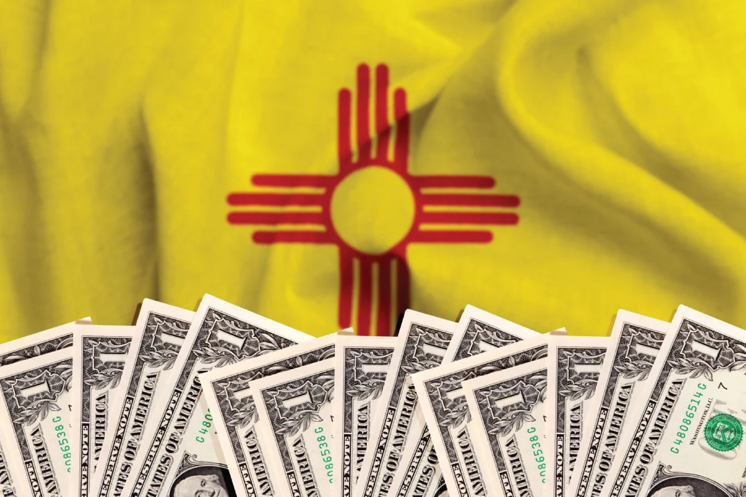 New Mexico flag in background with stacks of 1 dollar bills at foreground