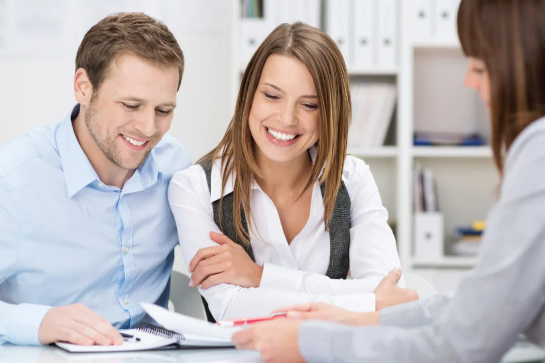 young couple sitting across from female loan provider signing documents