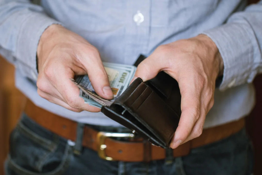 adult male placing stack of 100 dollar bills into his wallet